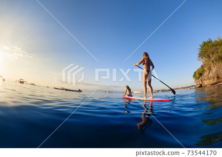 Young mother with little clild paddling on stand up paddleboard 73544170
