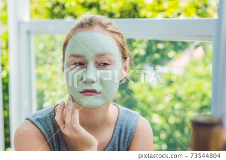 Spa Woman applying Facial green clay Mask. Beauty Treatments. Close-up portrait of beautiful girl applying facial mask Spa Woman applying Facial green clay Mask. Beauty Treatments. Close-up portrait of beautiful girl applying facial mask 73544804