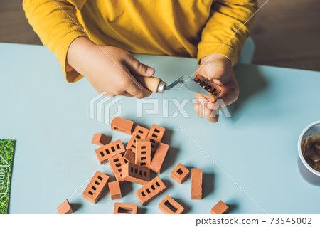 Close up of child's hands playing with real small clay bricks at the table. Toddler having fun and building out of real small clay bricks. Early learning. Developing toys. Construction concept Close up of child's hands playing with real small clay bricks at the table. Toddler having fun and building out of real small clay bricks. Early learning. Developing toys. Construction concept 73545002