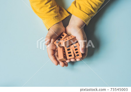 Close up of child's hands playing with real small clay bricks at the table. Toddler having fun and building out of real small clay bricks. Early learning. Developing toys. Construction concept Close up of child's hands playing with real small clay bricks at the table. Toddler having fun and building out of real small clay bricks. Early learning. Developing toys. Construction concept 73545003