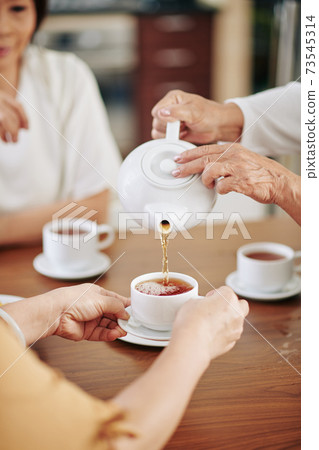 Senior woman pouring tea for guests Senior woman pouring tea for guests 73545314