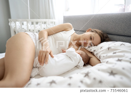 Beautiful woman breastfeeding her baby in a cozy house on the bed. 73546061