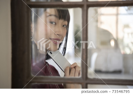 A view of a woman holding a smartphone through a window A view of a woman holding a smartphone through a window 73546795