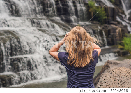 Young woman hiker, tourist on the background of Amazing Pongour Waterfall is famous and most beautiful of fall in Vietnam. Not far from Dalat city estimate 45 Km. Dalat, Vietnam 73548018