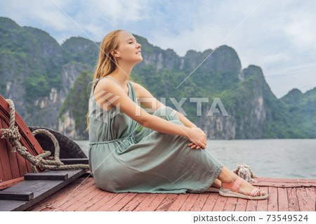 Attractive woman in a dress is traveling by boat in Halong Bay. Vietnam. Travel to Asia, happiness emotion, summer holiday concept. Picturesque sea landscape. Ha Long Bay, Vietnam 73549524
