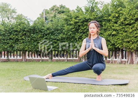 woman using laptop during online video training practicing yoga outdoors 73549816