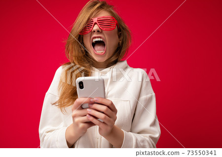Beautiful emotional young blonde woman wearing stylish white hoodie and funny colorful glasses 73550341