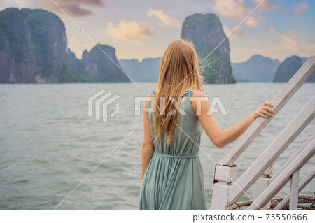 Attractive woman in a dress is traveling by boat in Halong Bay. Vietnam. Travel to Asia, happiness emotion, summer holiday concept. Picturesque sea landscape. Ha Long Bay, Vietnam 73550666
