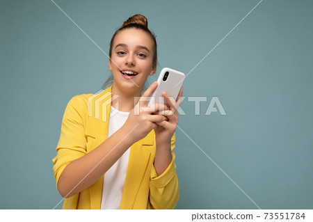 Beautiful young surprised girl wearing yellow jacket and white t-shirt standing isolated over blue 73551784