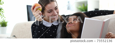 Two woman sit on couch near each other at home. Two woman sit on couch near each other at home. 73552136