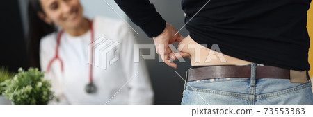 Man demonstrates cellulite on his sides to doctor. 73553383