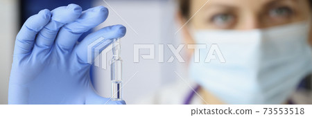 Doctor in rubber gloves and medical mask on face holding ampoule of medicine closeup Doctor in rubber gloves and medical mask on face holding ampoule of medicine closeup 73553518