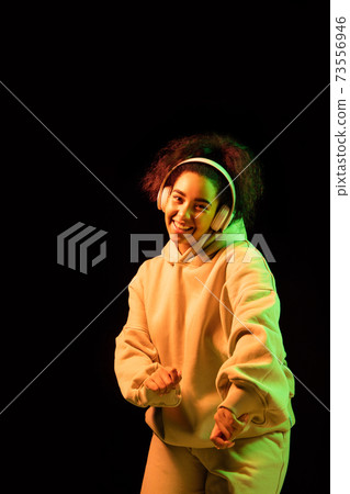 African-american woman's portrait isolated on dark studio background in orange-green neon light African-american woman's portrait isolated on dark studio background in orange-green neon light 73556946
