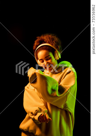 African-american woman's portrait isolated on dark studio background in orange-green neon light 73556962
