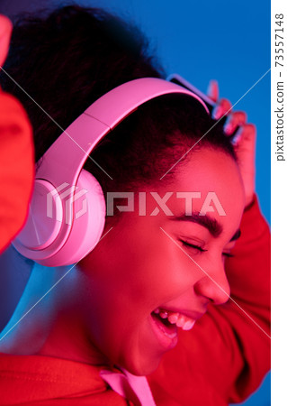 African-american woman's portrait isolated on blue studio background in multicolored neon light African-american woman's portrait isolated on blue studio background in multicolored neon light 73557148