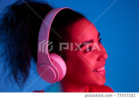 African-american woman's portrait isolated on blue studio background in multicolored neon light African-american woman's portrait isolated on blue studio background in multicolored neon light 73557281