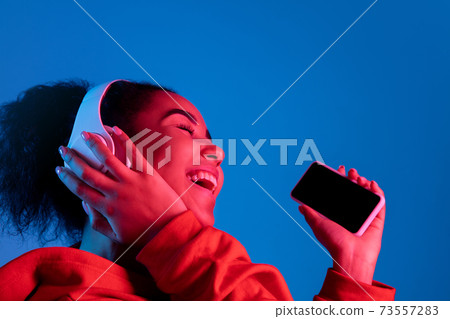 African-american woman's portrait isolated on blue studio background in multicolored neon light African-american woman's portrait isolated on blue studio background in multicolored neon light 73557283