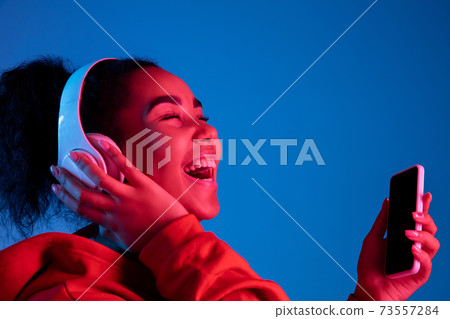 African-american woman's portrait isolated on blue studio background in multicolored neon light African-american woman's portrait isolated on blue studio background in multicolored neon light 73557284
