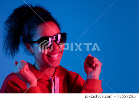 African-american woman's portrait isolated on blue studio background in multicolored neon light African-american woman's portrait isolated on blue studio background in multicolored neon light 73557286