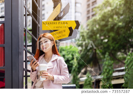 businesswoman wear pink suit holding smartphone and hot coffee cup walk on street. businesswoman wear pink suit holding smartphone and hot coffee cup walk on street. 73557287