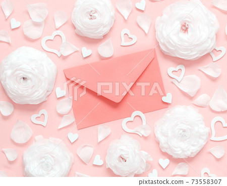 Pink envelope between cream flowers, petals and hearts on a light pink background 73558307