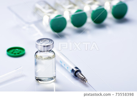 Just opened vial with liquid drug as vaccine ready dose flu shot along with syringe for injection treatment on medical table. Vaccination or immunization care concept background. Just opened vial with liquid drug as vaccine ready dose flu shot along with syringe for injection treatment on medical table. Vaccination or immunization care concept background. 73558398