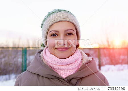 Portrait of beautiful girl at sunset in the winter. Smiling to camera, cheerful, true emotions. Winter fashion. 73559698