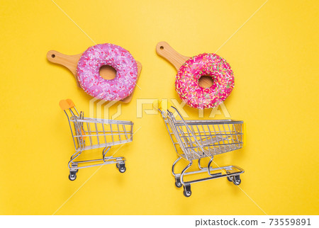 two Donuts with pink sugar glaze and sprinkled with colorful pastry crumbs, on a yellow background. the concept of shopping 73559891
