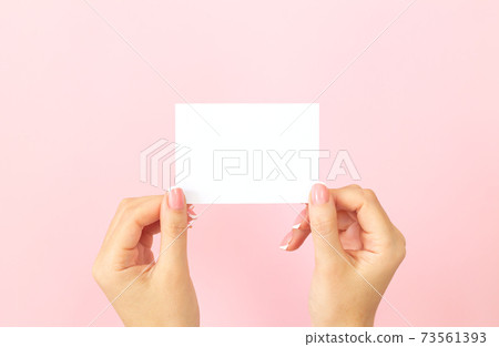 Female hands holding blank white business card on pink background Female hands holding blank white business card on pink background 73561393