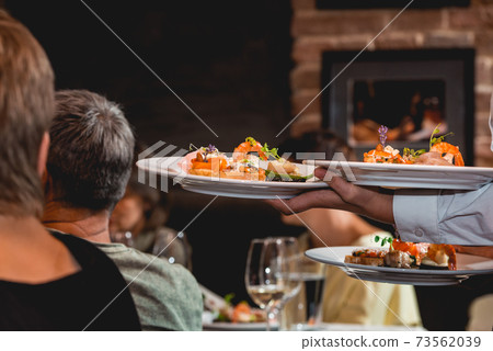 Waiter serves dish for food and wine tasting. Snacks with shrimp, fish fillets, Spain tapas recipe food pintxos Waiter serves dish for food and wine tasting. Snacks with shrimp, fish fillets, Spain tapas recipe food pintxos 73562039
