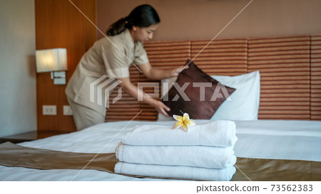 Plumeria and towels in front of hotel maid making the bed in the luxury hotel room ready for tourist travel 73562383