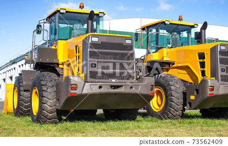 New and modern front loaders with large bucket and tipping cylinder. Engineering for construction and multifunctional tasks, background New and modern front loaders with large bucket and tipping cylinder. Engineering for construction and multifunctional tasks, background 73562409