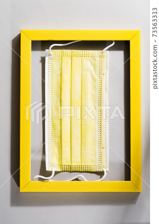 Yellow surgical face protection mask in the yellow frame on gray background. Trendy colors 2021. 73563313