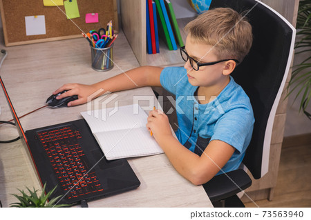 Schoolboy with glasses studies at home with laptop. Home learning, online education. 73563940