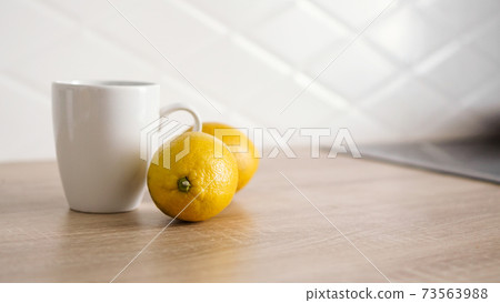 Two lemons on the kitchen table near a white mug of tea Two lemons on the kitchen table near a white mug of tea 73563988
