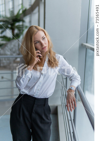 teenager talking on the phone. Beautiful with a lovely smile, webinar concept, on against the window, by the railing 73565491