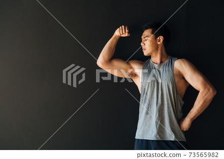 Focused young ethnic sportsman demonstrating biceps in studio 73565982