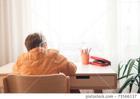 Cute 7 years old child doing his homework sitting by desk 73566137