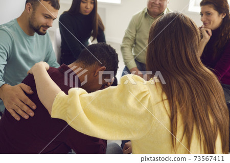 Friendly diverse people supporting an upset young man in a group therapy session 73567411