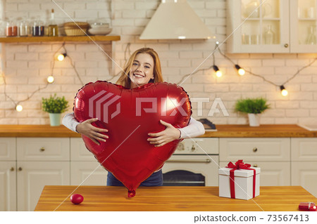 Portrait of a joyful girl hugging a big red heart shaped balloon looking at the camera. Portrait of a joyful girl hugging a big red heart shaped balloon looking at the camera. 73567413