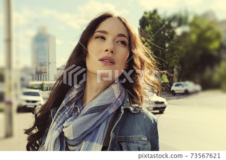 Portrait of a beautiful long-haired brunette in jeans with a scarf Portrait of a beautiful long-haired brunette in jeans with a scarf 73567621