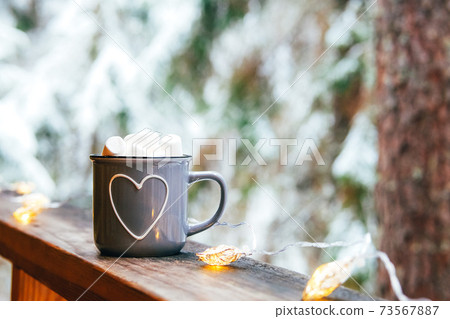 Gray mug with hot chocolate and marshmallow in winter landscape. 73567887