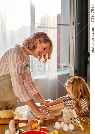 mother is teaching daughter to roll out dough 73567983