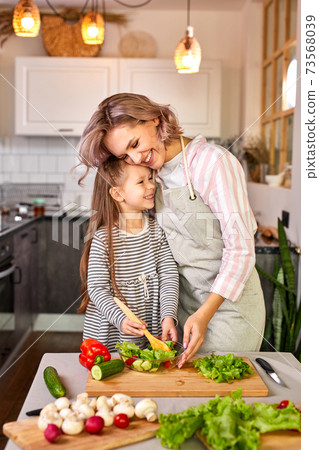 jolly child girl preparing a salad with her mother in the kitchen jolly child girl preparing a salad with her mother in the kitchen 73568039