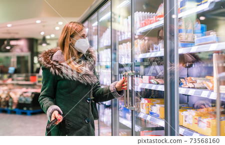 Woman at supermarket freezer section wearing face mask 73568160
