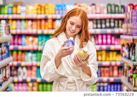 beautiful redhead female is comparing bath salts in the household goods department 73568229