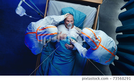 Top view of doctors and covid-19 patient with oxygen mask in bed in hospital, coronavirus concept. 73568291