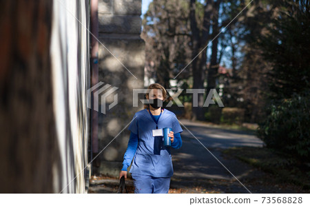 Woman caregiver, nurse or healthcare worker outdoors on the way to work, coronavirus concept. Woman caregiver, nurse or healthcare worker outdoors on the way to work, coronavirus concept. 73568828