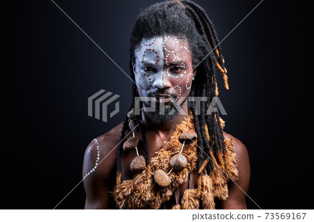 young black man with shaman aborigen make-up confidently looking at camera 73569167
