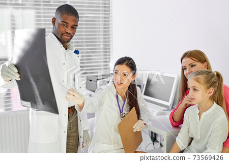 african male doctor and caucasian female assistant showing back x-ray to sick patients african male doctor and caucasian female assistant showing back x-ray to sick patients 73569426